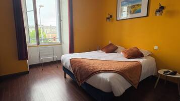Ein Schlafzimmer mit Bett, einem Fenster mit Vorhängen, einer Wandlampe und einem Bilderrahmen.