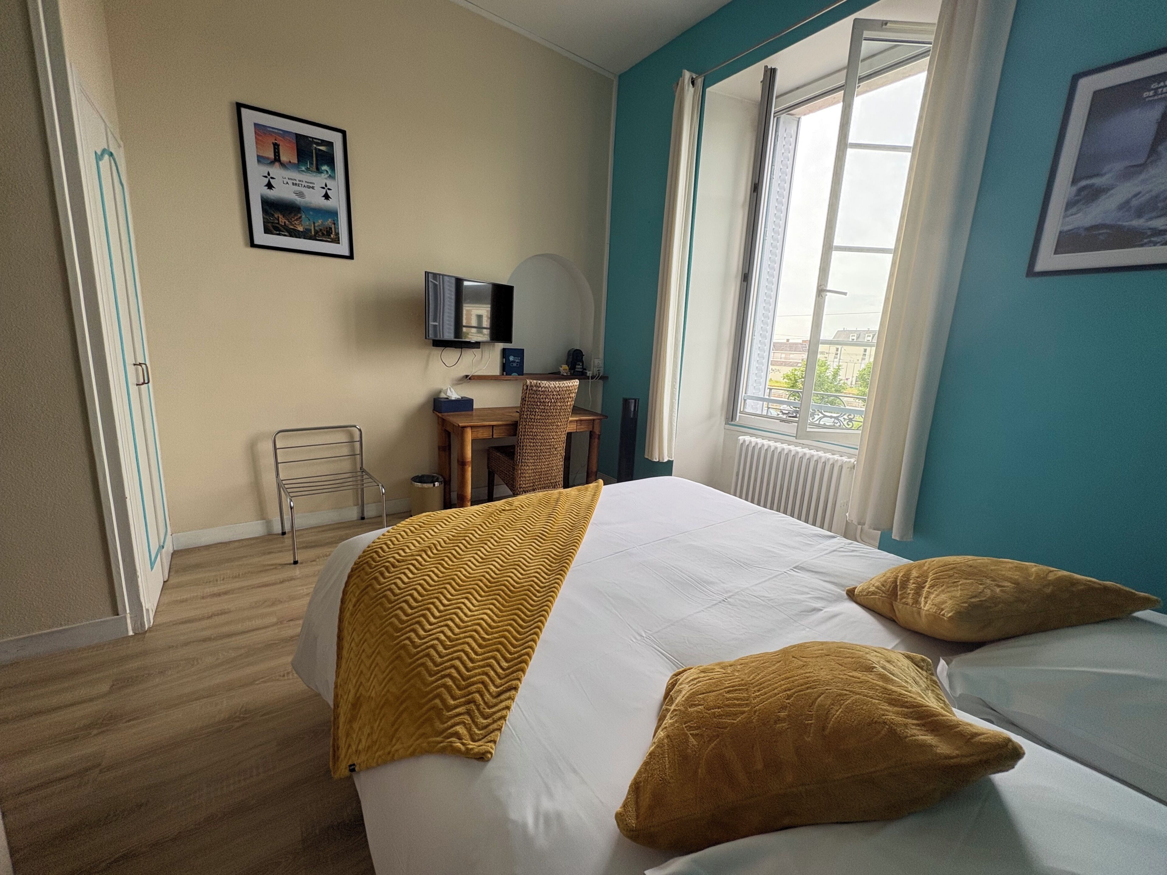 Une chambre d’hôtel équipée d’un lit, d’un bureau, d’une chaise, d’une fenêtre et d’un téléviseur fixé au mur.