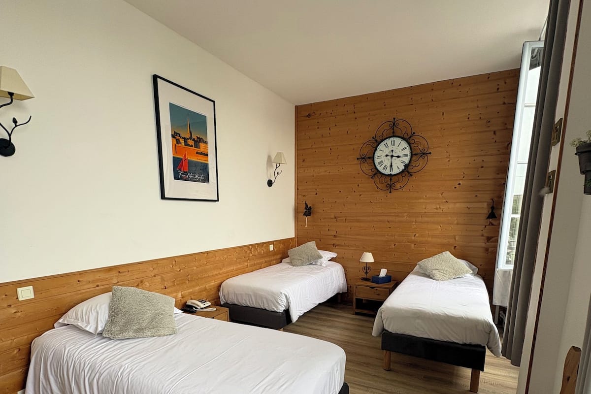 Ein Hotelzimmer mit zwei Betten, Holzboden, einer Wanduhr und einem gerahmten Bild.