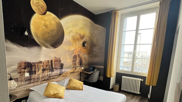 A hotel room with a bed, a desk, and a view of the city through a window. - Hôtel de Bretagne (Redon)