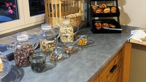 A breakfast bar with various food items, including jars of granola, chocolate chips, and nuts, and a wicker basket. - Hôtel de Bretagne (Redon)