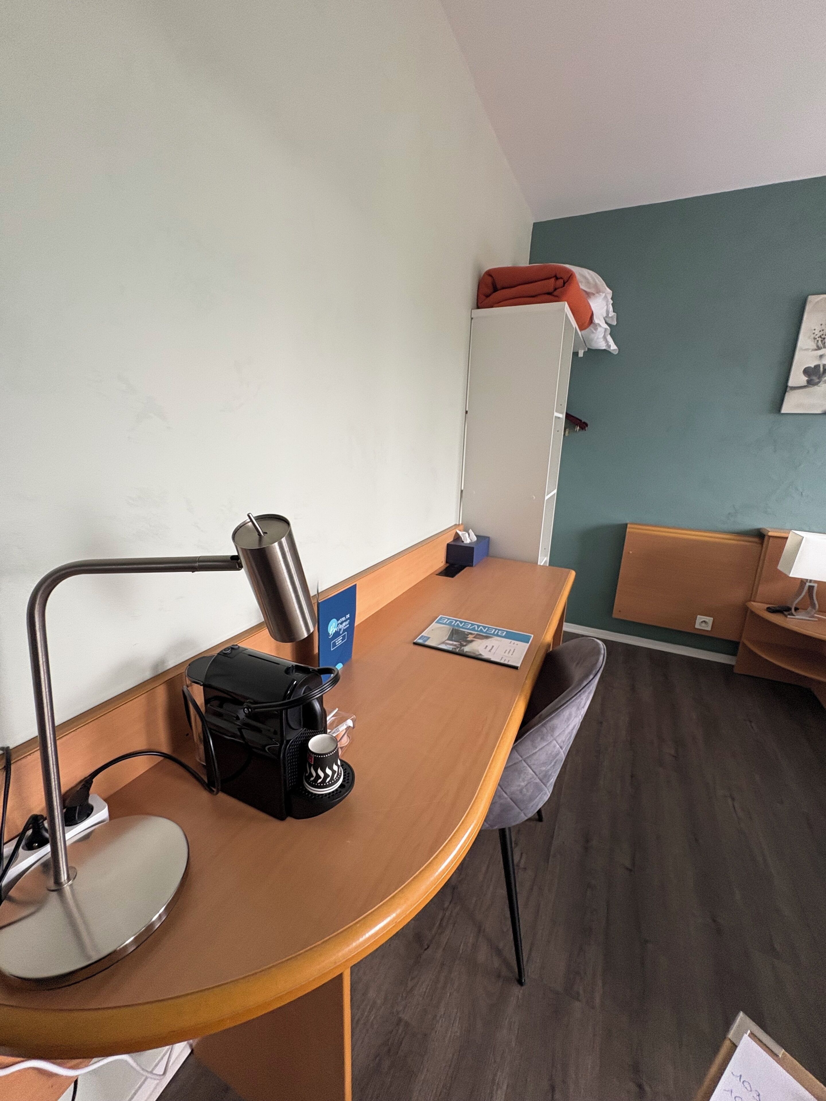 Habitación de hotel con un escritorio de madera, cafetera, sillón, cama y mueble de pared.