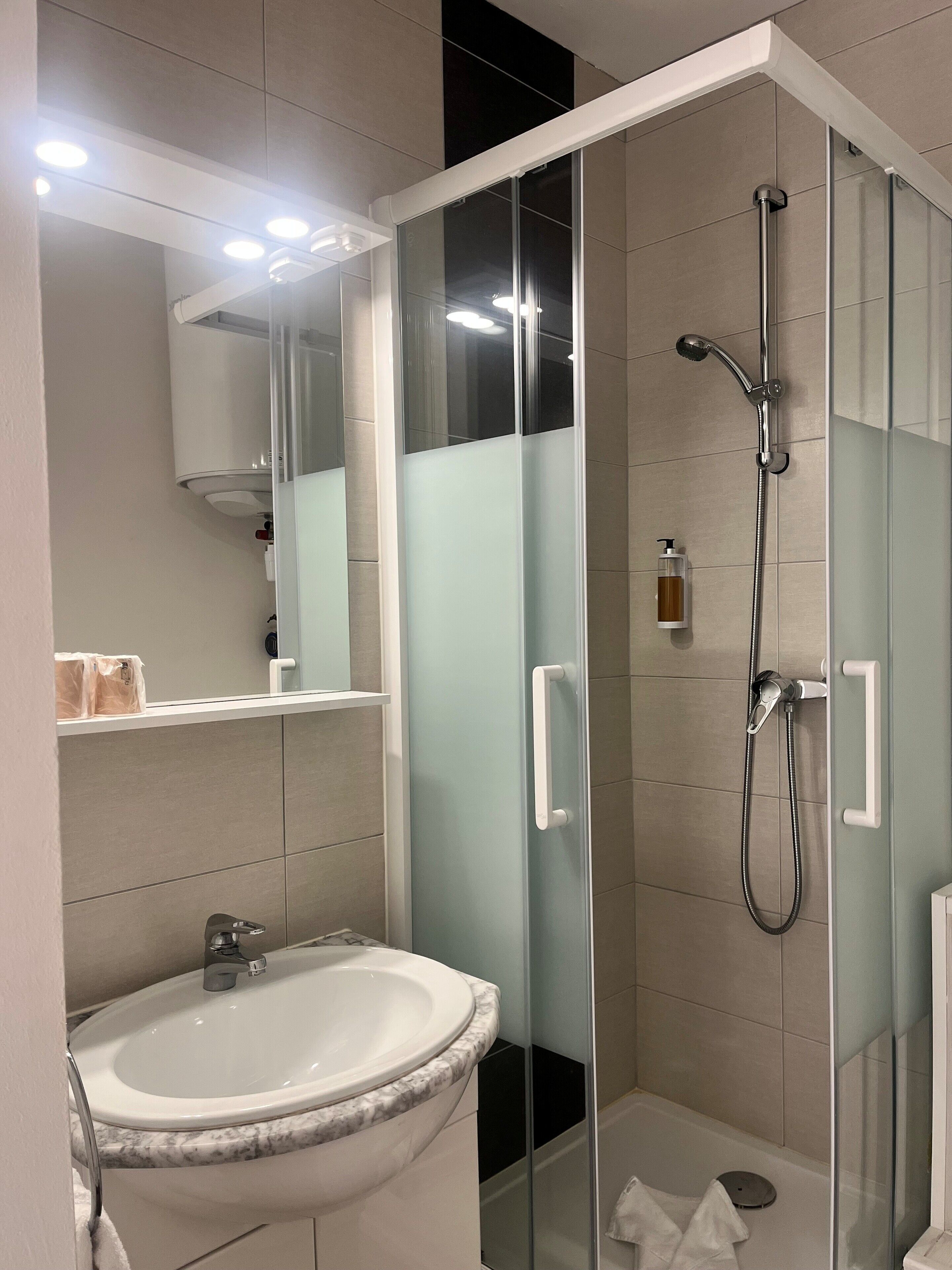 Un baño moderno con ducha envuelta en vidrio, un lavamanos blanco con encimera de mármol y un espejo sobre el lavamanos.