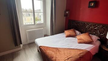 Una habitación de hotel con una cama, un ventanal con cortinas, un radiador y una pared roja.