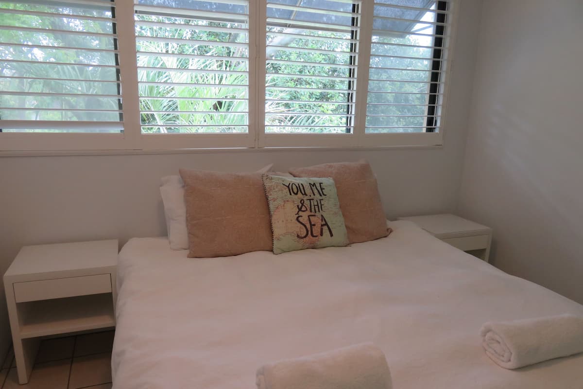 A neatly made bed with a pillow that reads "YOU ME & THE SEA".