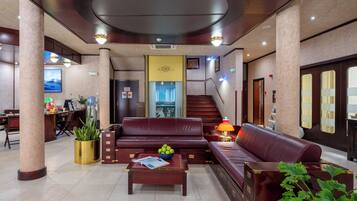 A spacious lobby with a red leather sofa, a coffee table with magazines, and a staircase leading to the upper floors.