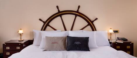Una cama bien hecha con cabecera de madera, dos mesitas de noche con lámparas y dos almohadas con texto.