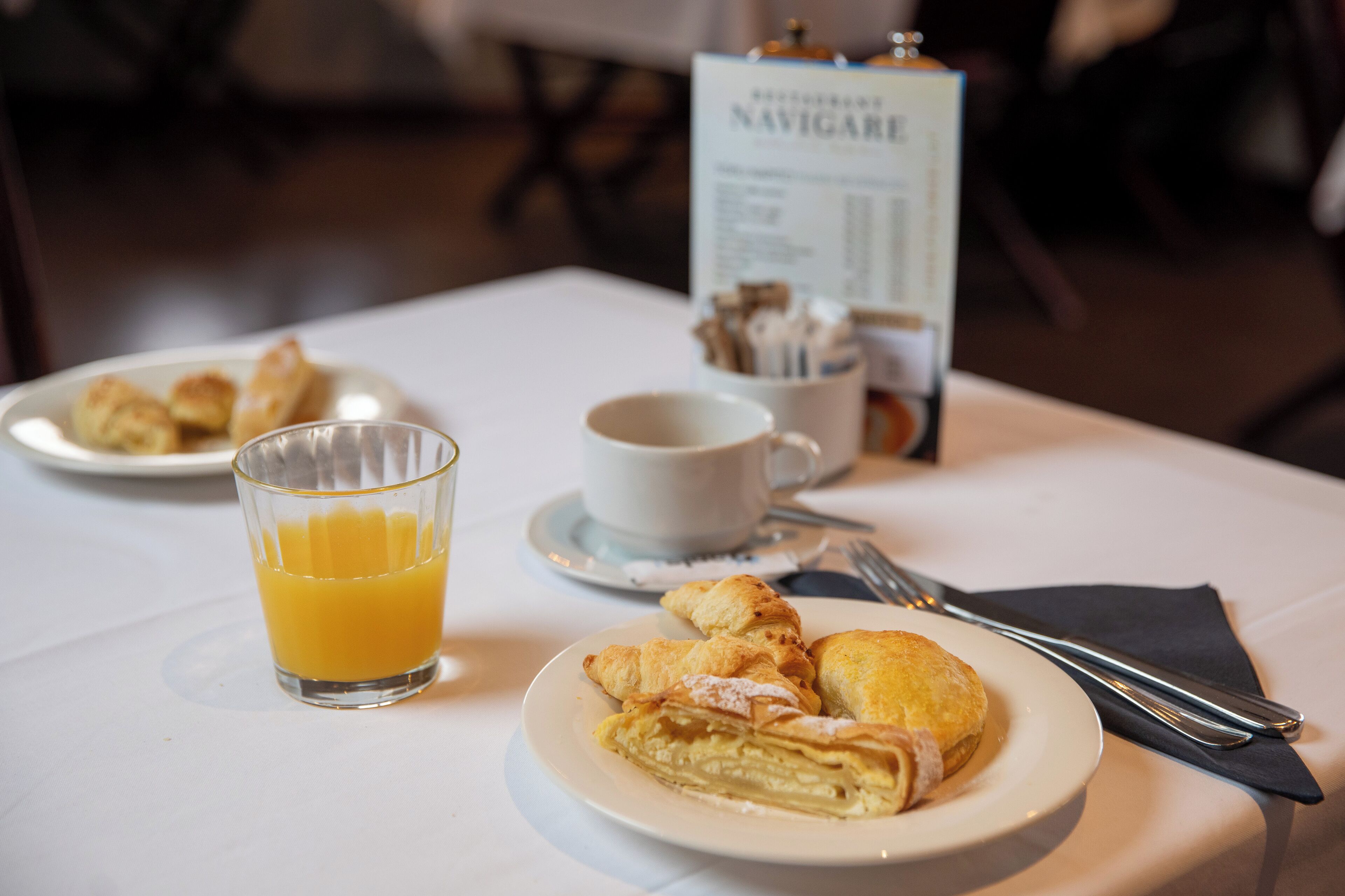Un desayuno con croissants, un vaso de zumo de naranja y un cartel de menú.