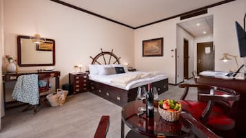 A hotel room with a bed, bedside table, desk, chair, and a dining table with a fruit bowl and wine glasses.