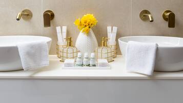 A bathroom with two sinks, a vase with yellow flowers, and toiletries on the counter.