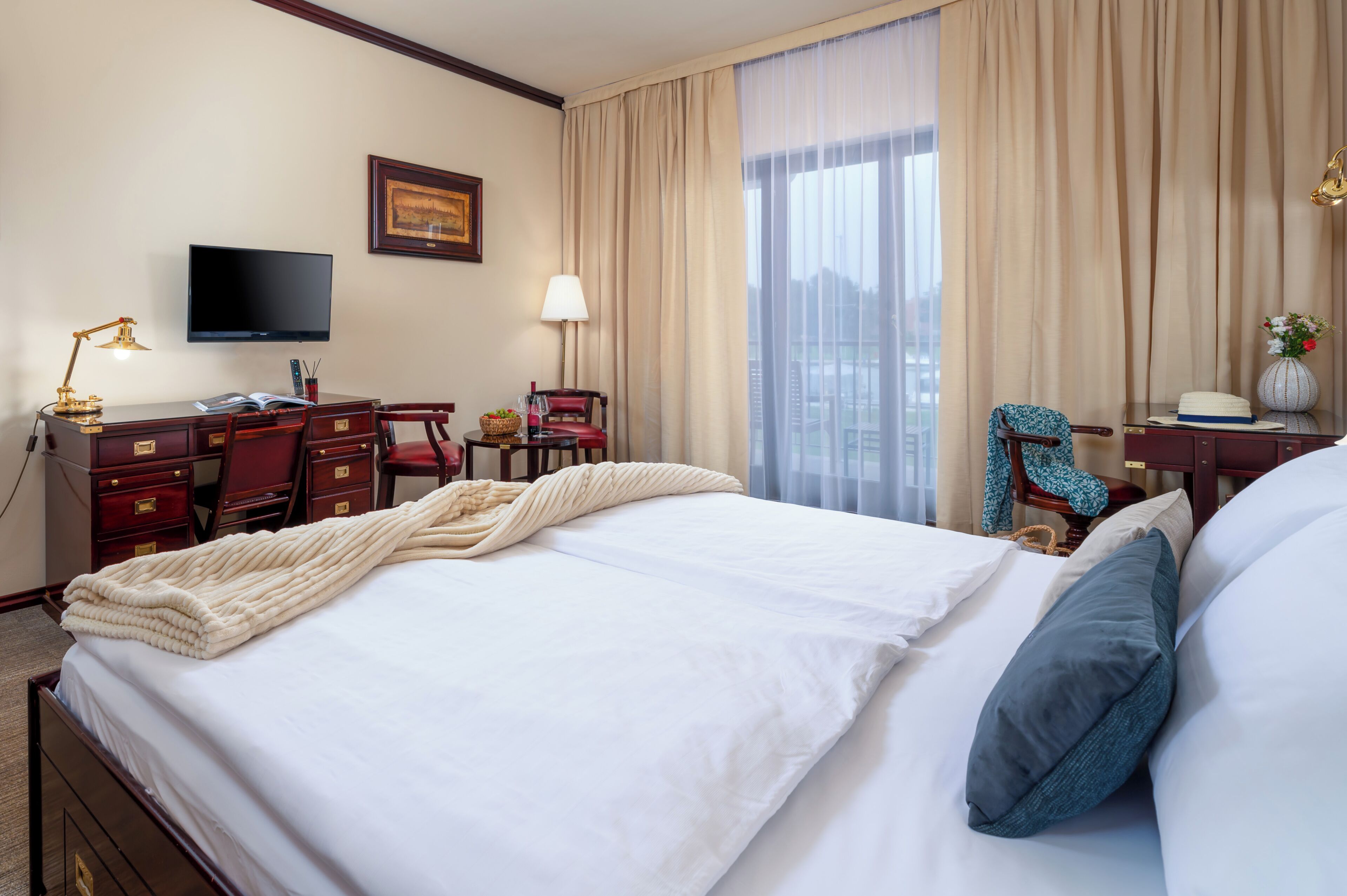 A hotel room with a large bed, a desk with a computer, a television, and a view of the city.