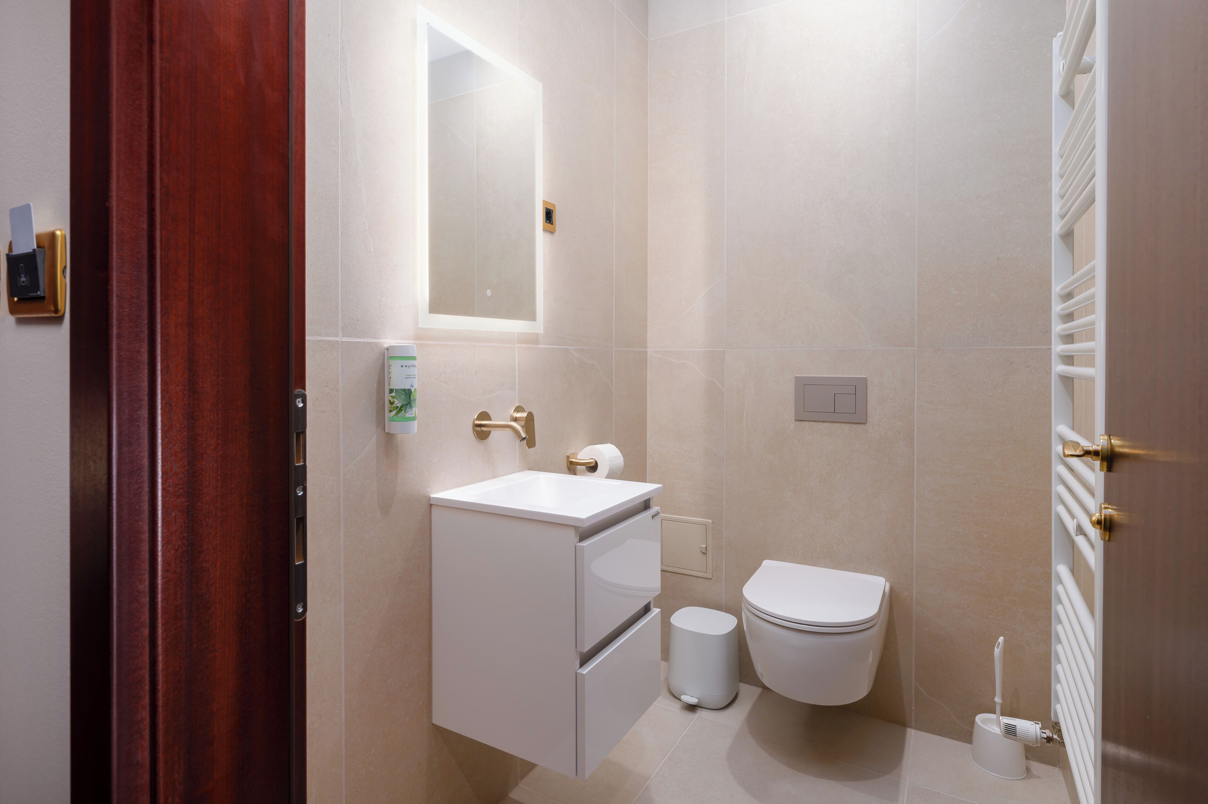 Un baño moderno con puerta de madera, lavamanos blanco, inodoro y barra para toallas.