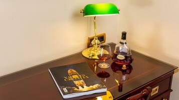 A wooden desk with a green desk lamp, a bottle of liquor, a glass, and a book titled "Yachts Croatia".