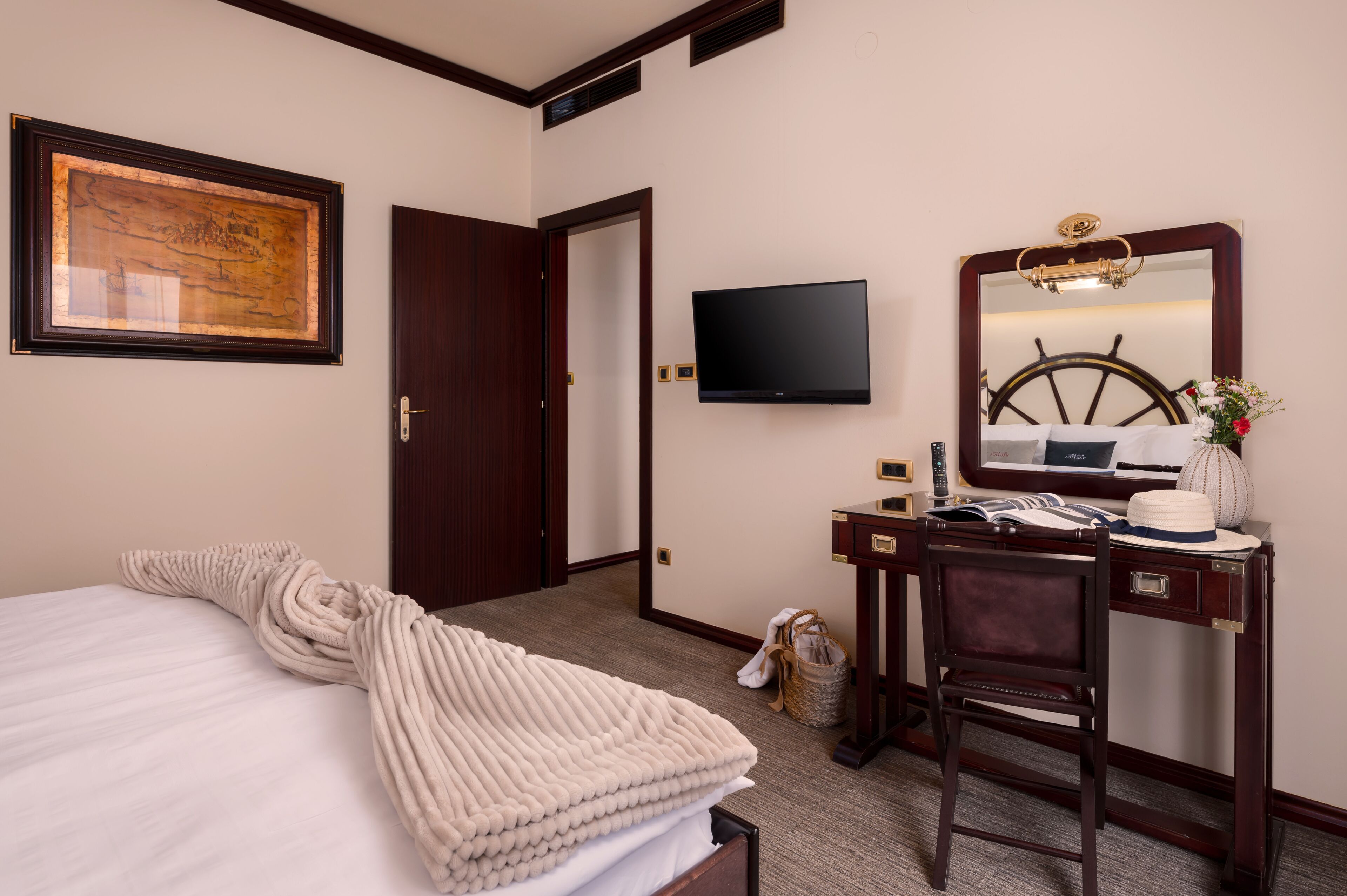 A hotel room with a bed, a desk with a computer, a television, and a large mirror.