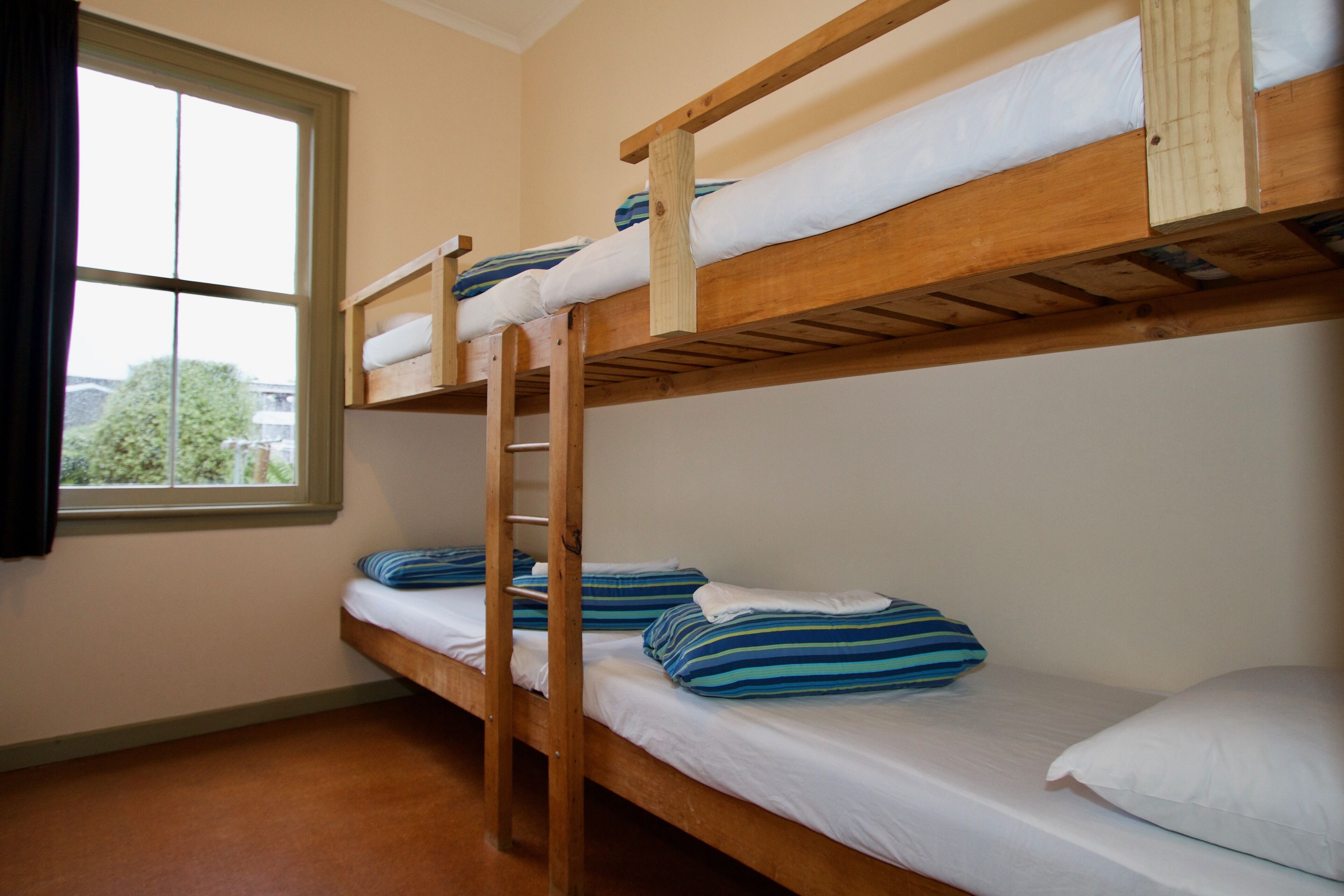 Habitación con literas, ventana, literas de madera y almohadas a rayas.