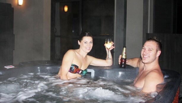 Un hombre y una mujer en un jacuzzi con una botella de champán.