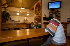 Un restaurante acogedor con muebles de madera, un televisor mostrando un reporte del clima y un recorte decorativo de un árbol en la pared.