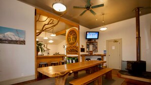 Una mesa de comedor de madera con bancos, un ventilador de techo, un televisor y un estufa de leña.