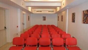 A conference room with rows of red chairs, white walls, and a carpeted floor.