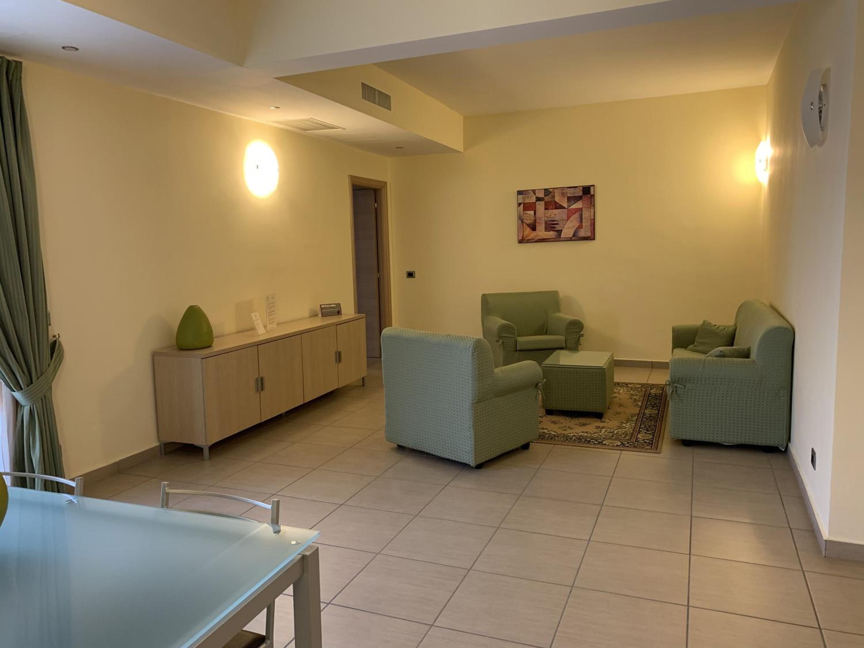 Una sala de estar con una mesa de vidrio, dos sillones, un sofá, un aparador y un cuadro en la pared.