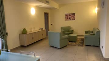 Una sala de estar con una mesa de vidrio, dos sillones, un sofá, un aparador y un cuadro en la pared.