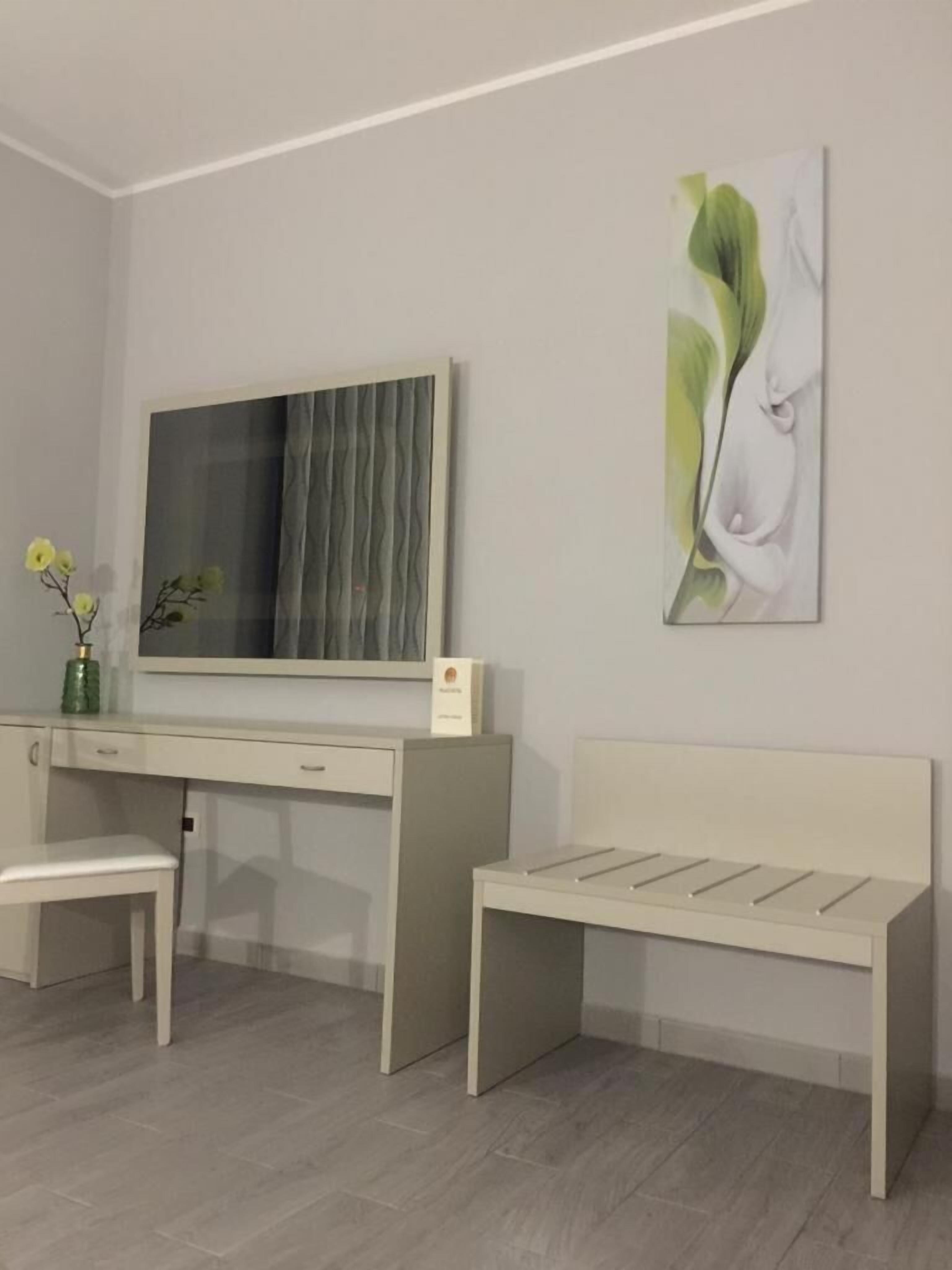 A modern room with a desk, a bench, a large mirror, and a wall-mounted artwork.