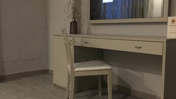 Una habitación moderna con un televisor de pantalla plana grande montado en la pared, un escritorio blanco con una silla y un tapete estampado en el suelo.
