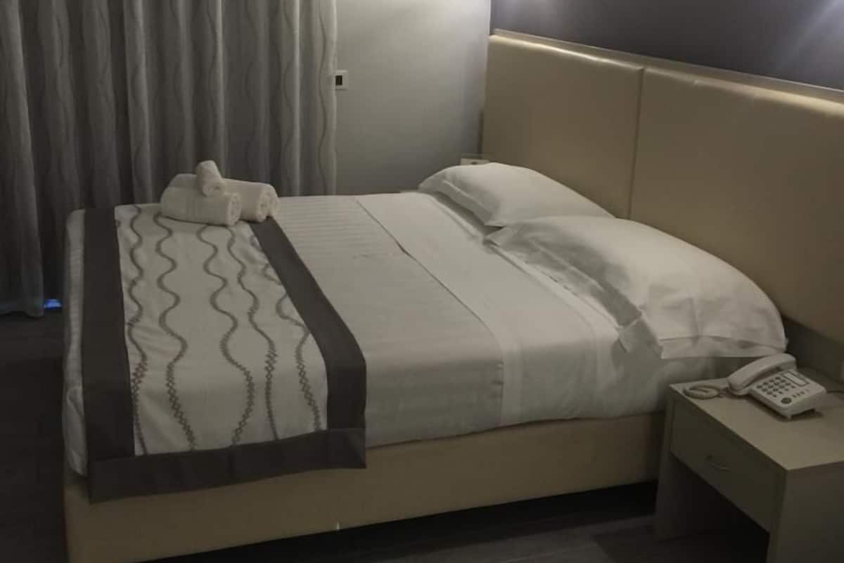 Una habitación de hotel con una cama, una mesita de noche con teléfono y una cortina.