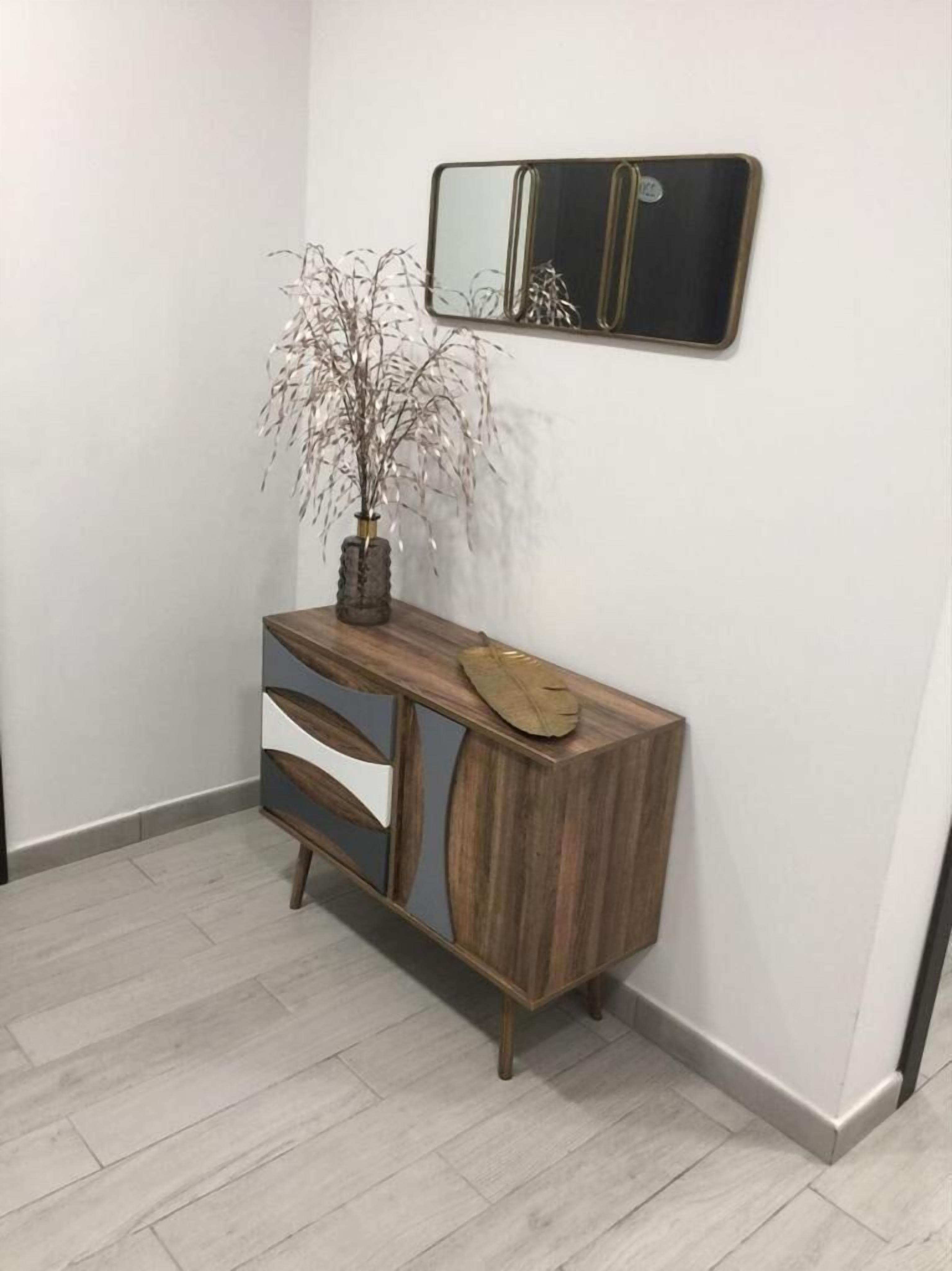 Un angolo di una stanza con un tavolino consolle in legno, un vaso con dei rami e uno specchio appeso al muro.