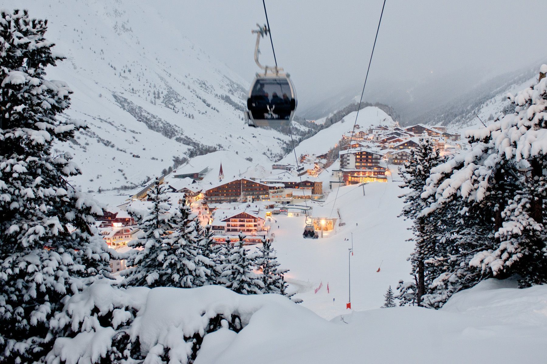 A snow-covered mountain village with buildings and a ski lift.
