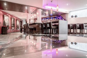 A modern bar area with a polished reflective floor, dark wooden bar counter, and multiple bar stools. - Josl Mountain Lounging Hotel (Soelden)