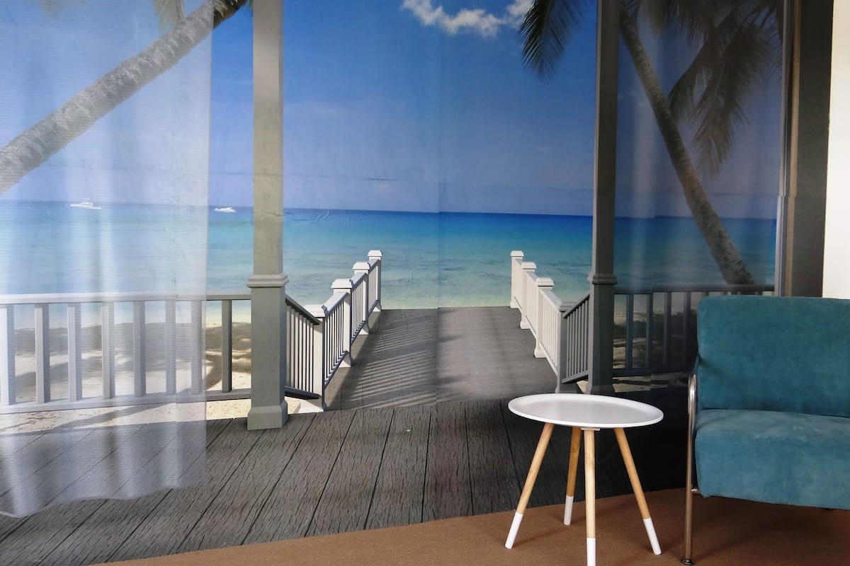 A room with a beach mural, a wooden deck, a white table, and a blue chair.