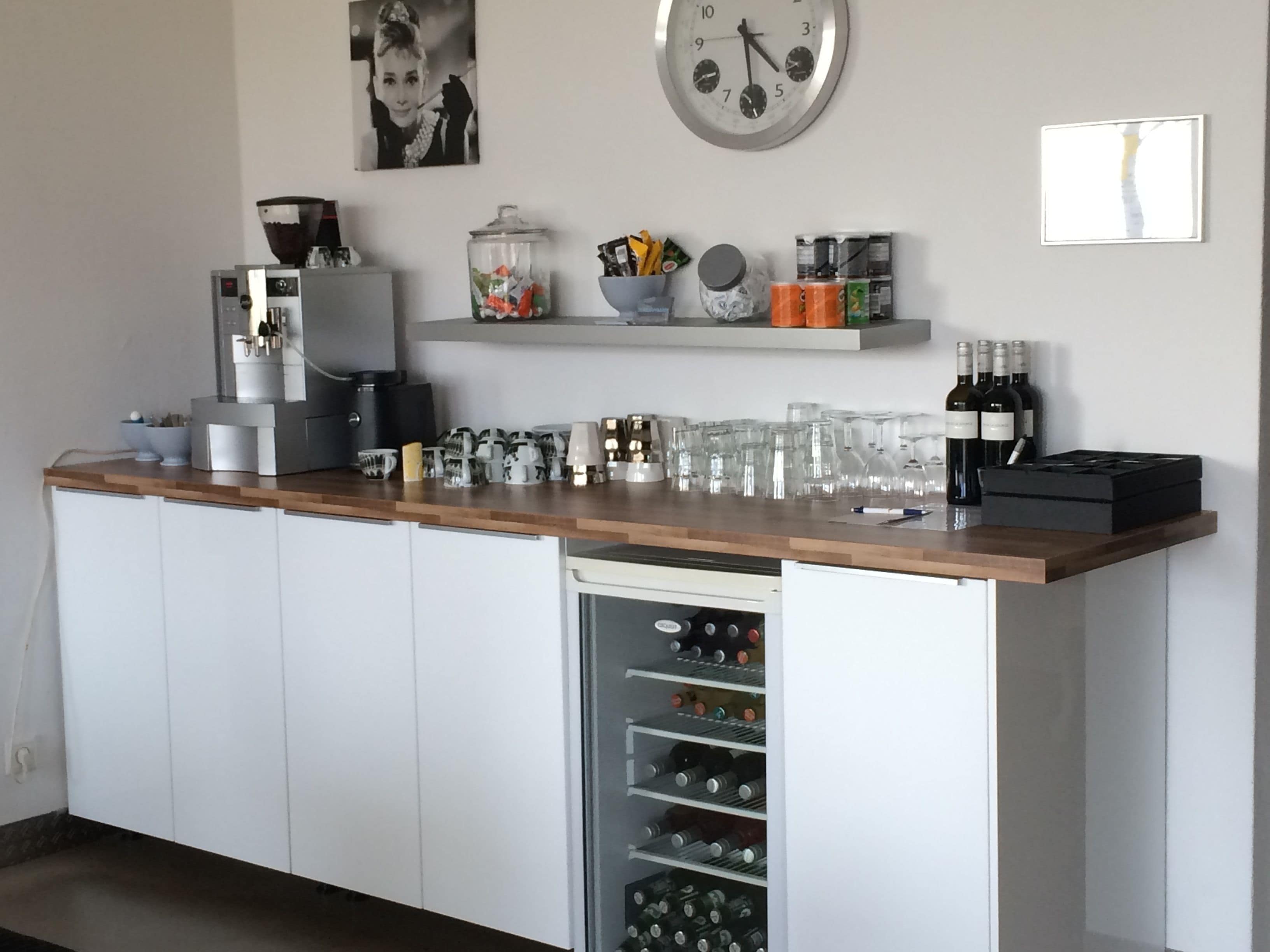 A kitchen with a wooden countertop, a coffee machine, a wine cooler, and various kitchen utensils.