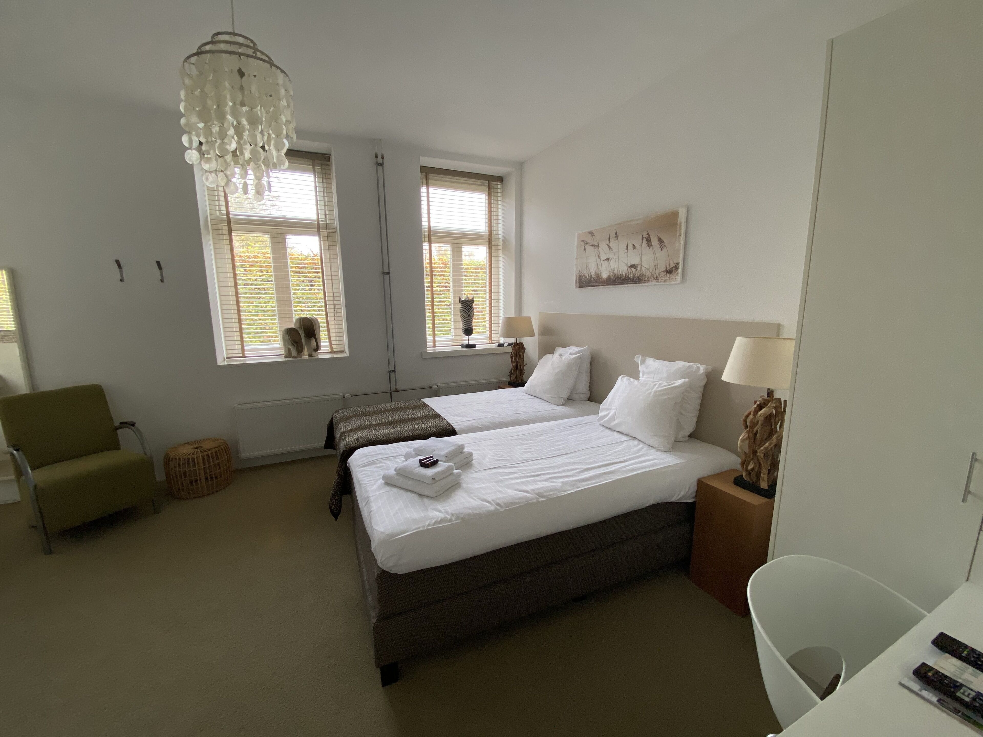 A hotel room with two beds, a green chair, a small table, and a chandelier.