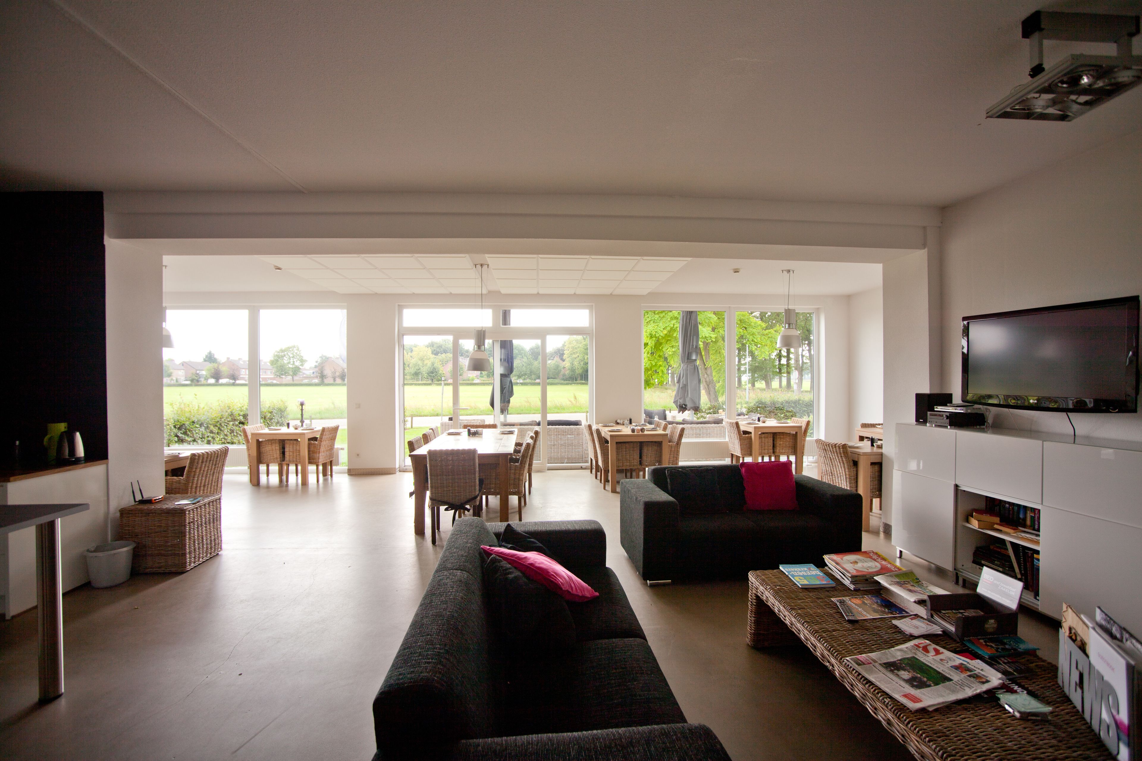 Ein geräumiges Wohnzimmer mit einer großen Couch, einem Essbereich mit Stühlen, einem Fernseher und Blick ins Freie.