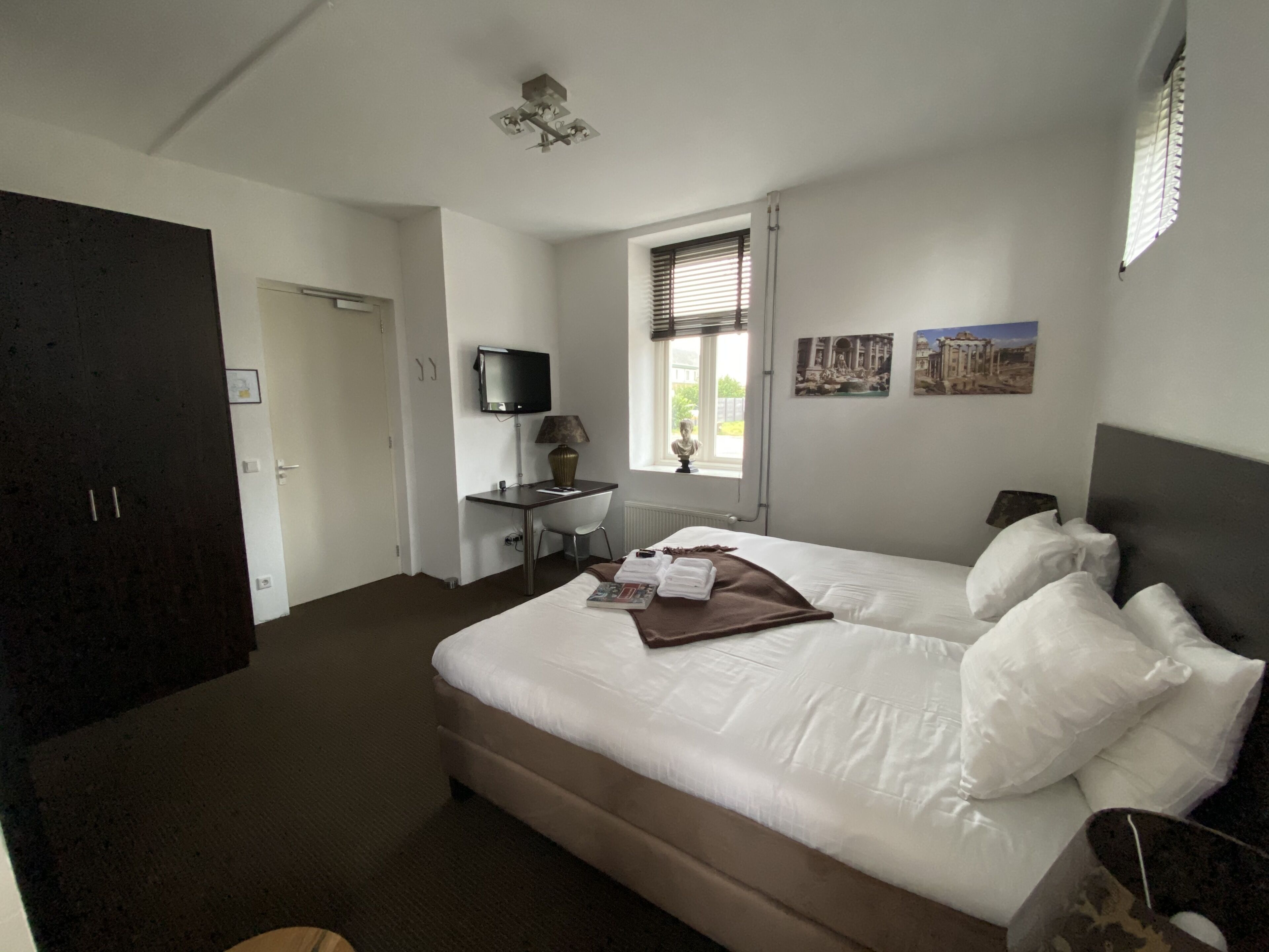 Ein Schlafzimmer mit einem Bett, einem Schreibtisch, einem Fernseher und einem Fenster mit Jalousien.