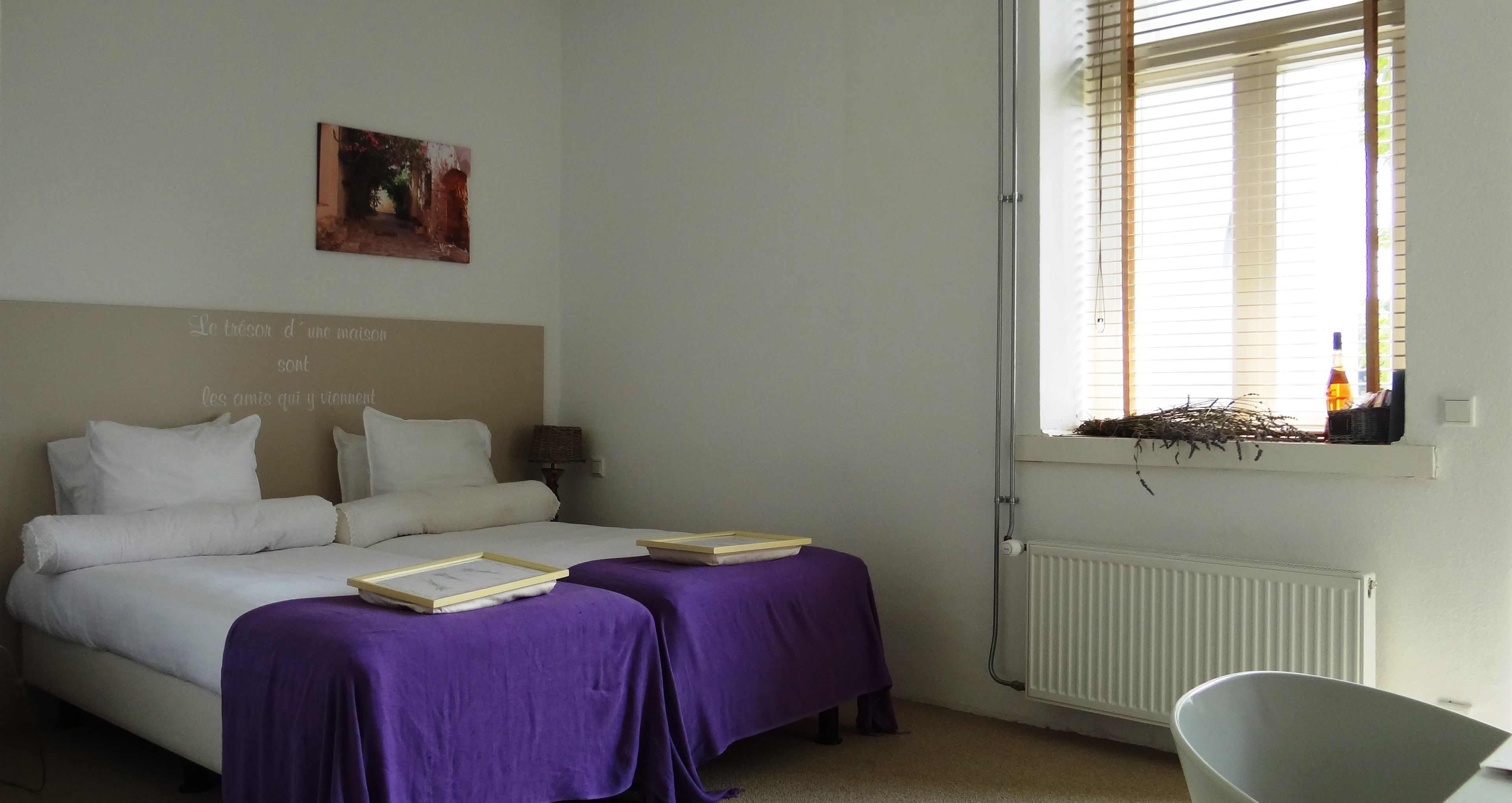 Un dormitorio con dos camas, una ventana con persianas, un radiador y una mesita con un libro.