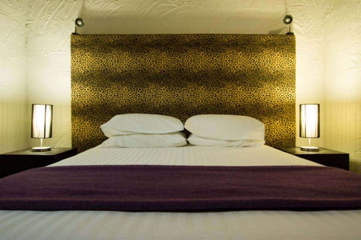 A hotel room with a bed, two bedside tables, and a patterned headboard.