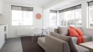 A modern, well-lit living room with a grey sofa, a coffee table, and a dining area with a white table and chairs. - Silverski (Falls Creek)