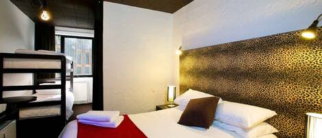 Una habitación de hotel con una cama litera, un cabecero estampado de leopardo, una manta roja y una lámpara de noche.