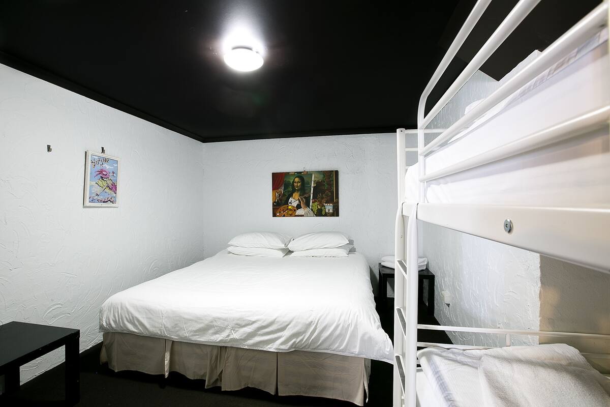 A single-bed room with a white bed, a small bedside table, and a wall-mounted shelf.