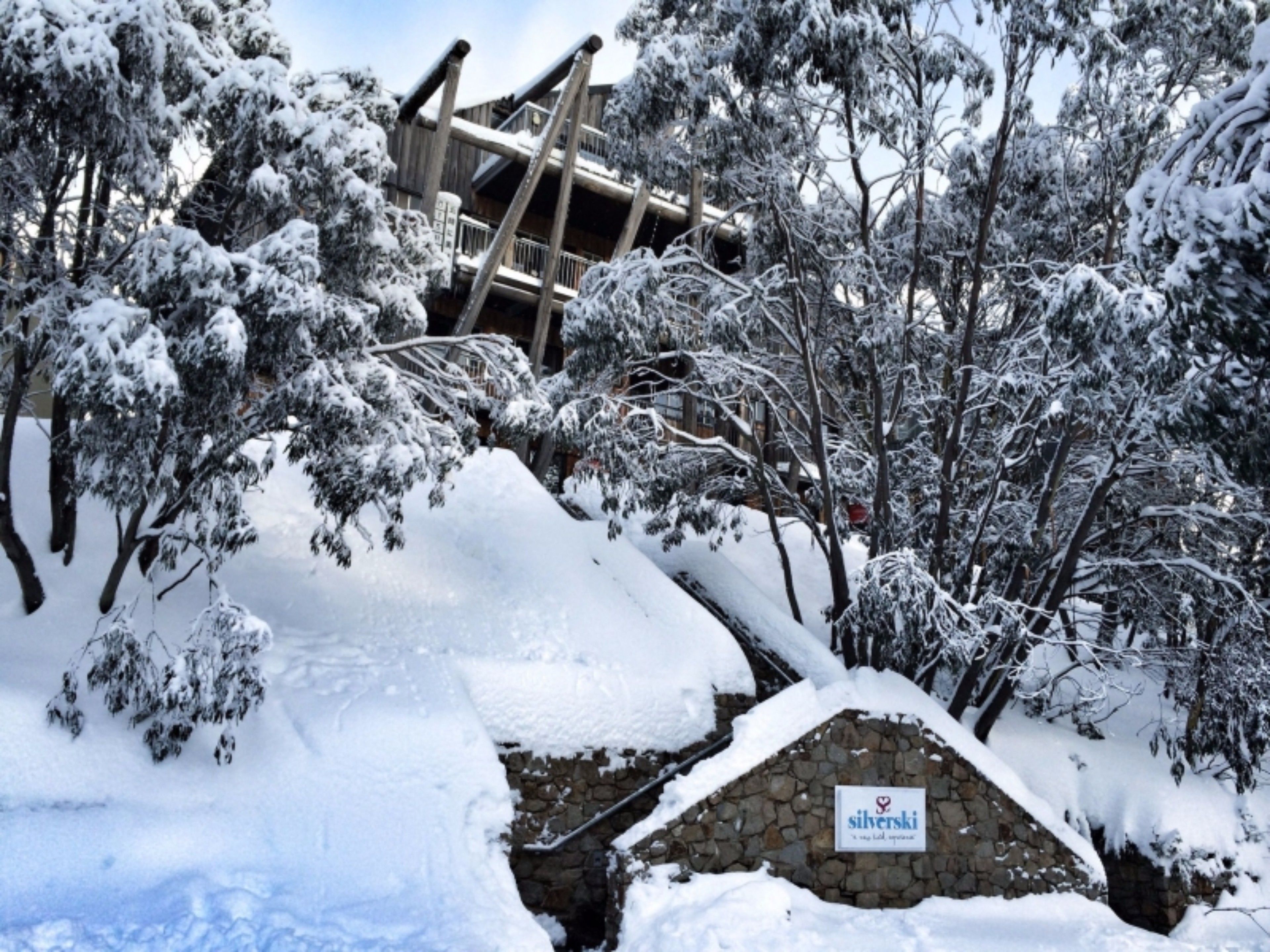A snow-covered building with a stone wall and a sign that reads "silverski."