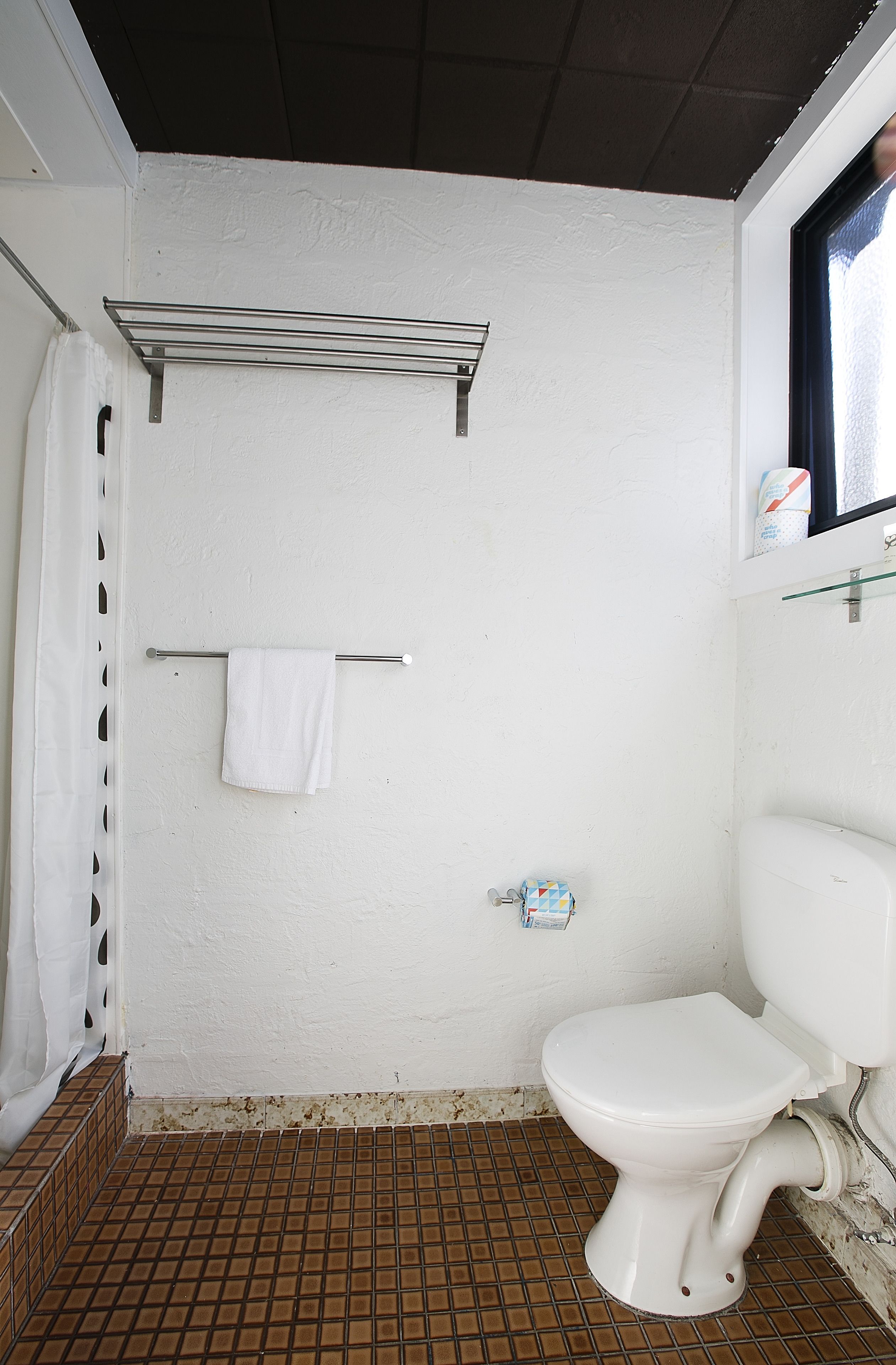 Une petite salle de bain blanche, équipée de toilettes, d’un porte-serviettes et d’un rideau de douche.