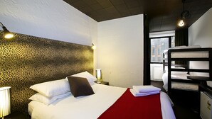 A hotel room with a bed, a red throw blanket, a nightstand with a lamp, and a bunk bed. - Silverski (Falls Creek)