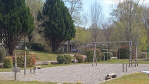 A playground with a swing set and climbing structure, surrounded by trees and a gravel path. - Terres de France - Les Hameaux de Miel (Beynat)