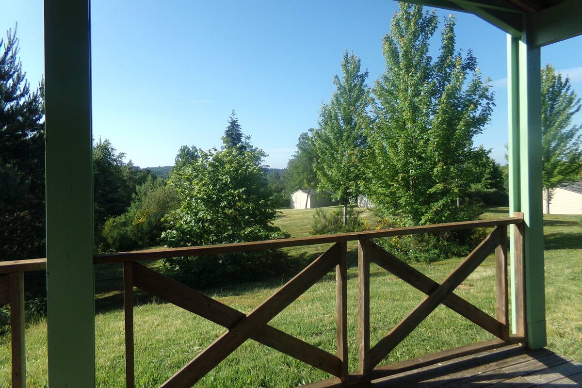 Uma área externa coberta com guarda-corpo de madeira, um gramado e árvores ao fundo.