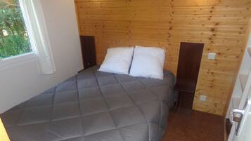 A bedroom with a wooden ceiling, a bed with grey bedding, a nightstand, and a window with curtains.