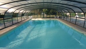 An indoor swimming pool with a curved roof, clear water, and white chairs along the sides. - Terres de France - Les Hameaux de Miel (Beynat)