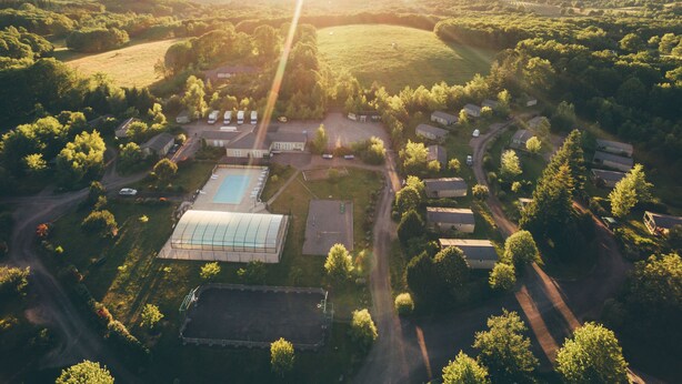 An aerial view of a residential area with a large swimming pool, multiple houses, and a greenhouse. - Terres de France - Les Hameaux de Miel (Beynat)