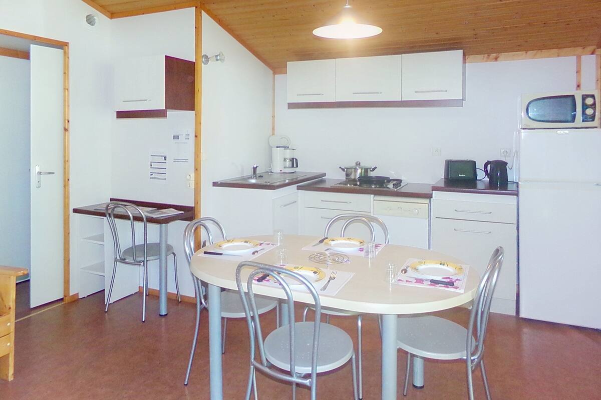 Cozinha compacta com armários brancos, micro-ondas e mesa de jantar com cadeiras.